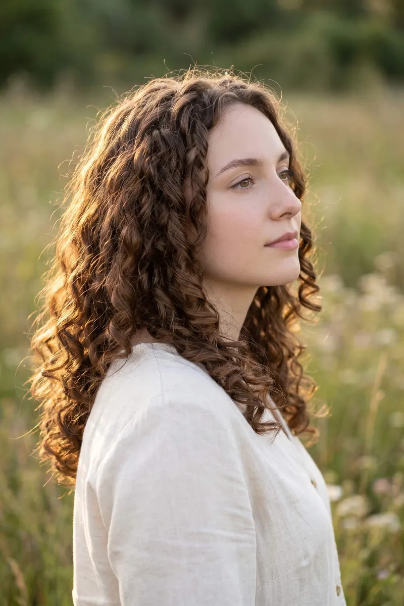 Woman with long defined brown ringlets in warm evening light